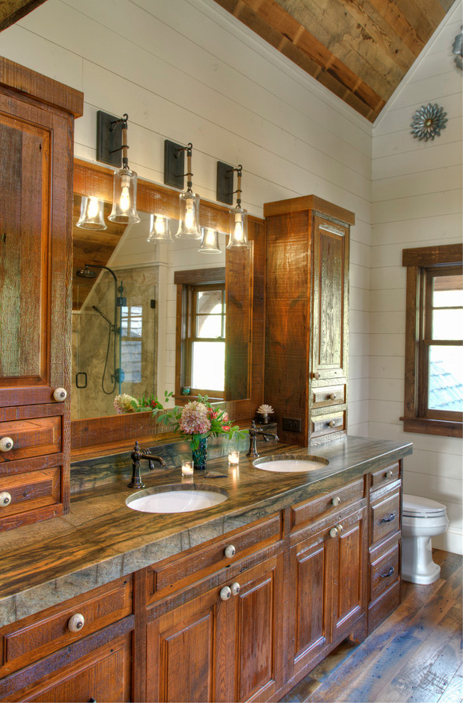 Photo of a large country master bathroom in Minneapolis with raised-panel cabinets, dark wood cabinets, white walls, dark hardwood floors, an undermount sink, granite benchtops, brown floor, a hinged shower door and green benchtops.