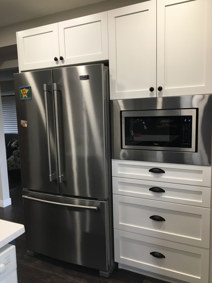 Example of a mid-sized transitional u-shaped dark wood floor and brown floor kitchen design with a farmhouse sink, shaker cabinets, white cabinets, quartzite countertops, white backsplash, subway tile backsplash, stainless steel appliances, an island and gray countertops