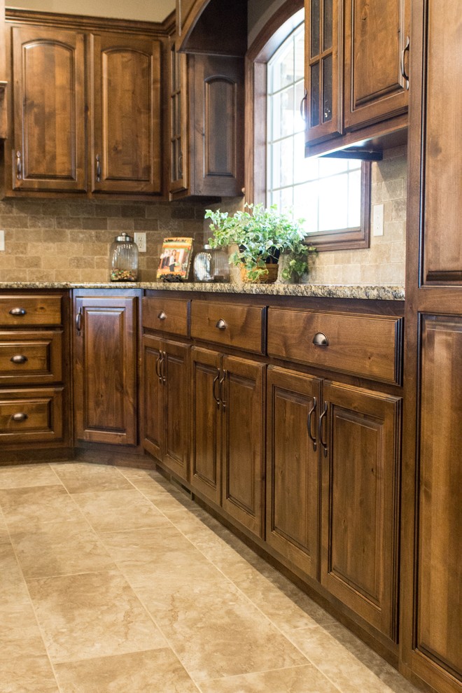 Photo of a mid-sized country u-shaped separate kitchen in Other with an undermount sink, raised-panel cabinets, dark wood cabinets, granite benchtops, beige splashback, stone tile splashback, stainless steel appliances, travertine floors, with island, beige floor and beige benchtop.