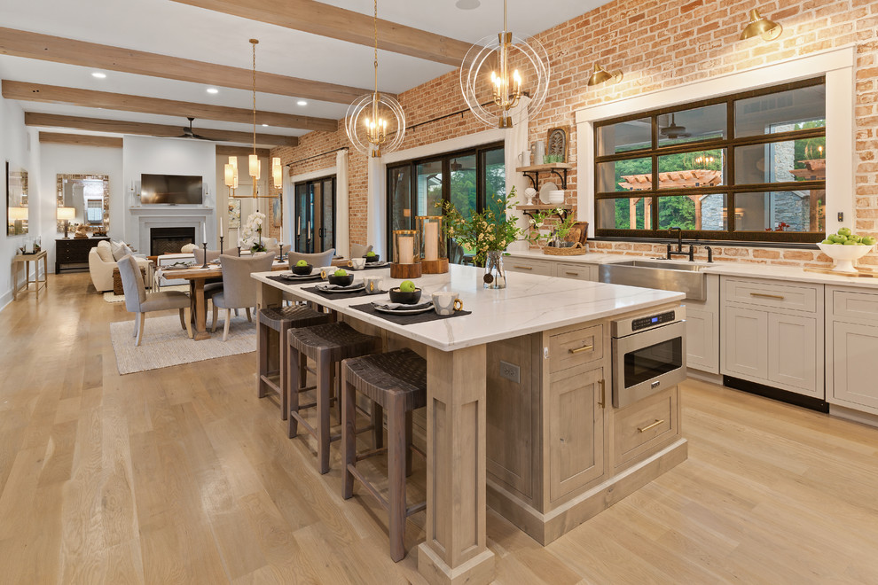 Country open plan kitchen in Cincinnati with a farmhouse sink, shaker cabinets, grey cabinets, red splashback, brick splashback, stainless steel appliances, light hardwood floors, with island, beige floor and white benchtop.