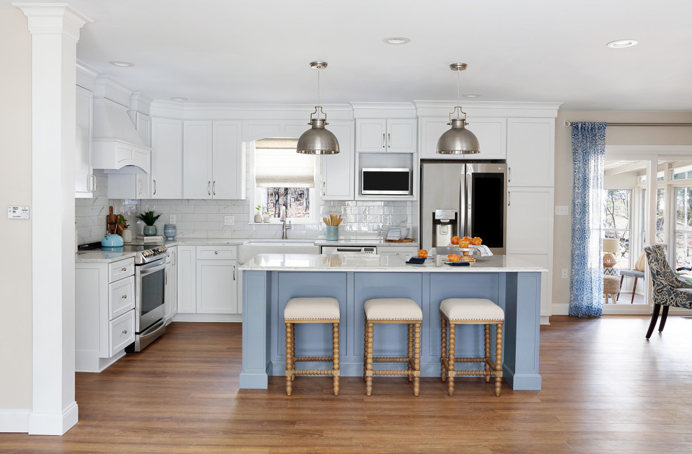Design ideas for a traditional l-shaped open plan kitchen in Philadelphia with a belfast sink, shaker cabinets, white cabinets, engineered stone countertops, white splashback, ceramic splashback, stainless steel appliances, vinyl flooring, an island, brown floors and white worktops.