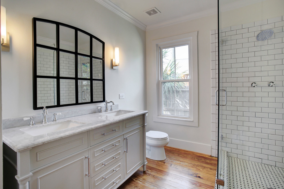 Mid-sized country master bathroom in Houston with beaded inset cabinets, white cabinets, a freestanding tub, a corner shower, a one-piece toilet, subway tile, white walls, medium hardwood floors, an undermount sink, marble benchtops, a hinged shower door and brown floor.