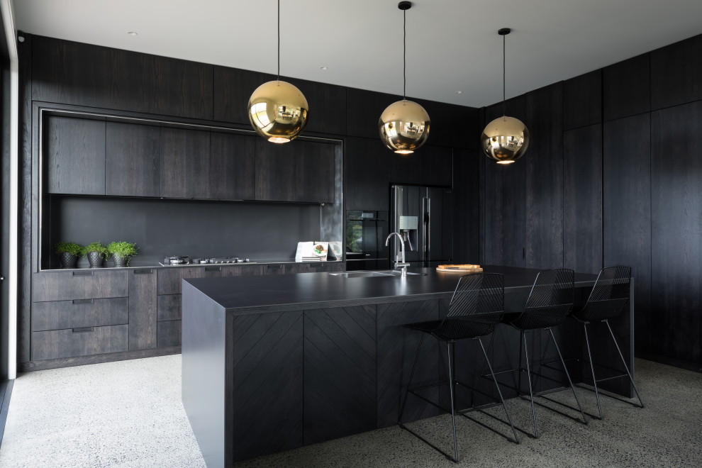 Large contemporary kitchen in Auckland with black splashback, concrete floors, with island, black benchtop, a double-bowl sink, flat-panel cabinets, black cabinets, stainless steel appliances and multi-coloured floor.