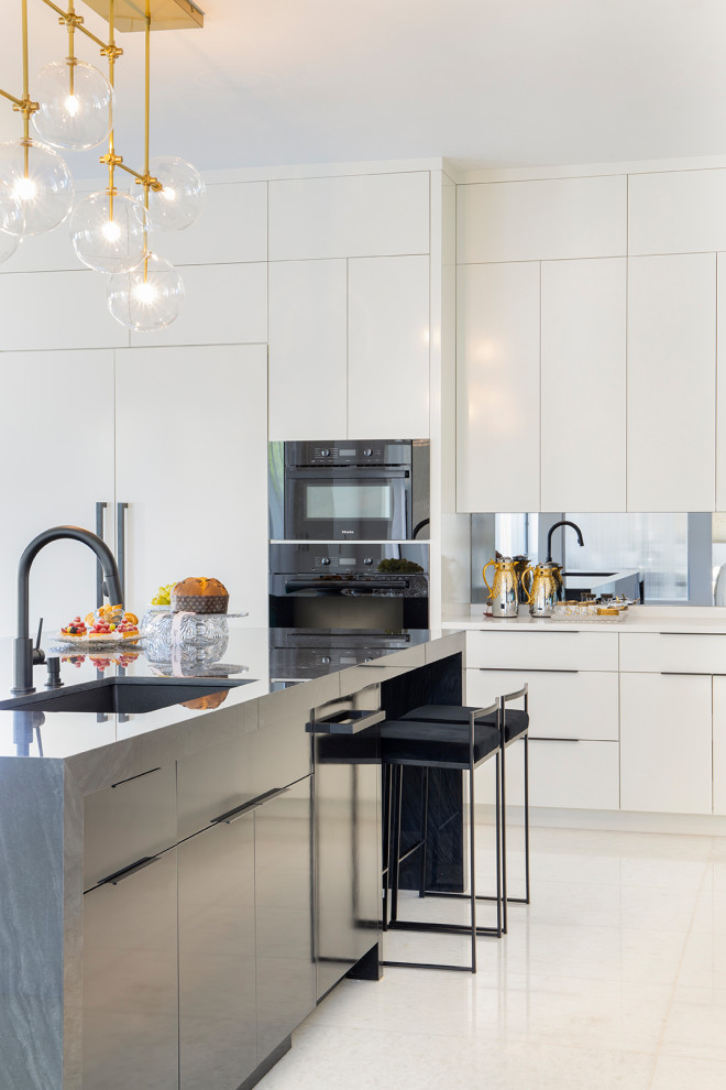 This is an example of a large modern l-shaped open plan kitchen in Miami with an undermount sink, flat-panel cabinets, white cabinets, marble benchtops, grey splashback, mirror splashback, black appliances, marble floors, with island, white floor and black benchtop.