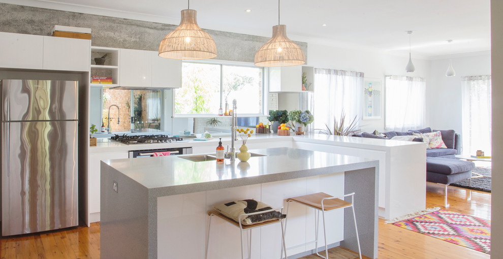 Inspiration for a contemporary l-shaped open plan kitchen in Sydney with a double-bowl sink, flat-panel cabinets, white cabinets, stainless steel appliances, medium hardwood floors, with island, brown floor and grey benchtop.