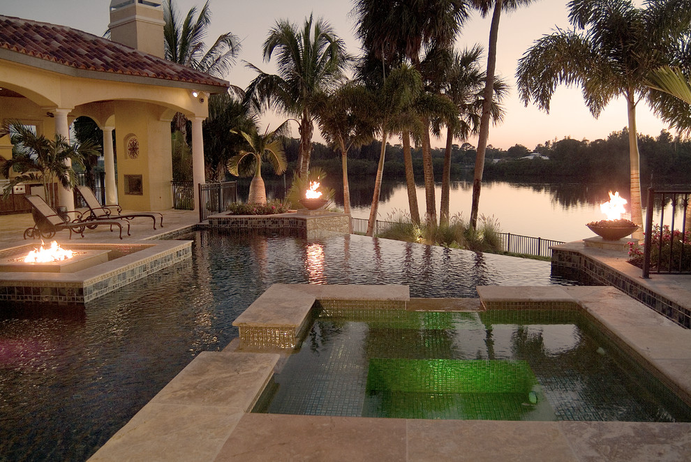 Photo of a large contemporary backyard custom-shaped infinity pool in Tampa with a water feature and natural stone pavers.