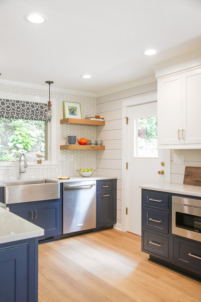 Small beach style u-shaped separate kitchen in Milwaukee with a farmhouse sink, recessed-panel cabinets, blue cabinets, quartz benchtops, white splashback, porcelain splashback, stainless steel appliances, light hardwood floors and beige benchtop.