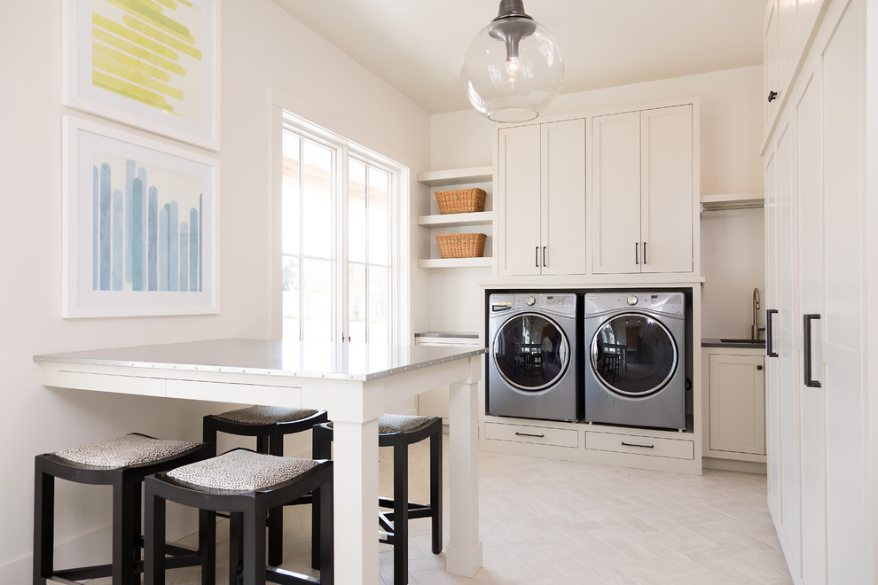 This is an example of a large contemporary utility room in Other with an undermount sink, beige cabinets, stainless steel benchtops, beige walls, ceramic floors, a side-by-side washer and dryer and beige floor.