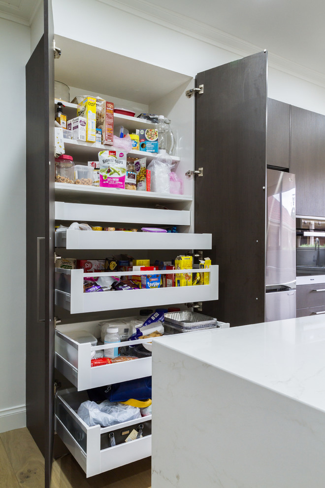 Photo of a large contemporary u-shaped eat-in kitchen in Melbourne with a drop-in sink, flat-panel cabinets, white cabinets, quartz benchtops, metallic splashback, glass sheet splashback, black appliances, light hardwood floors, with island, brown floor and white benchtop.