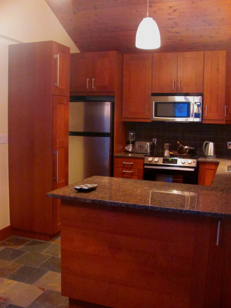 Example of a mid-sized mountain style u-shaped slate floor kitchen design with an undermount sink, shaker cabinets, medium tone wood cabinets, granite countertops, black backsplash, ceramic backsplash, stainless steel appliances and a peninsula