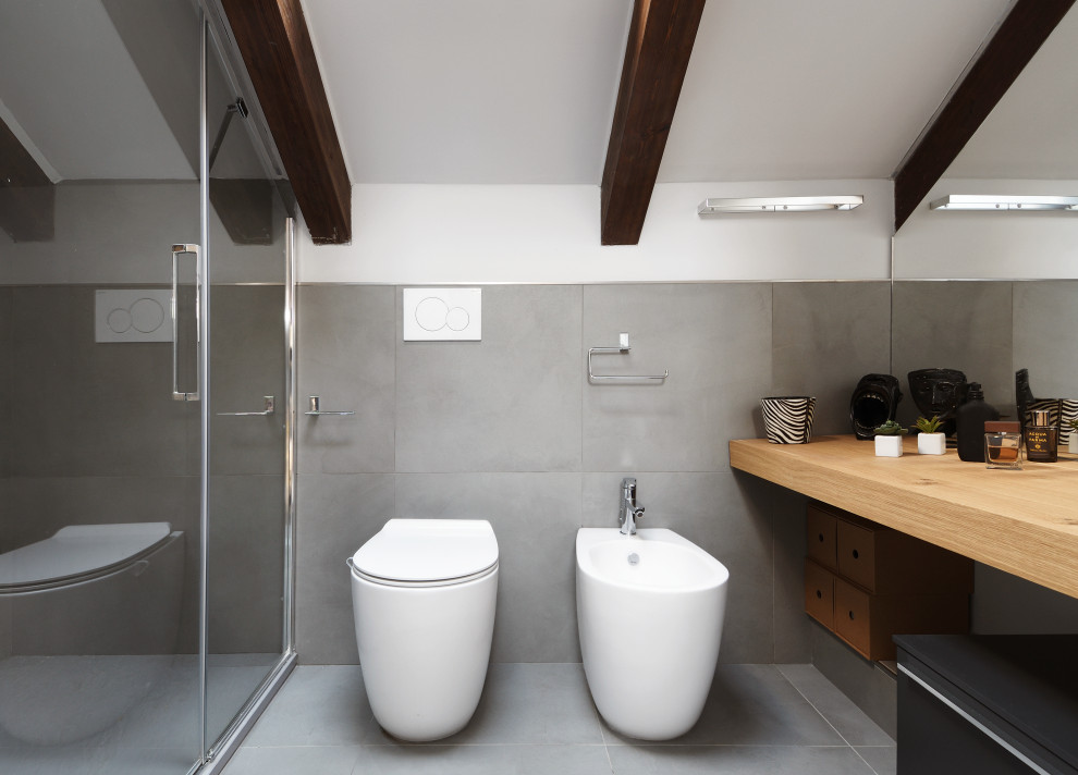 Photo of an expansive contemporary bathroom in Turin with gray tile, porcelain tile, porcelain floors, wood benchtops, a hinged shower door, light wood cabinets, a double shower, a two-piece toilet, a vessel sink and flat-panel cabinets.