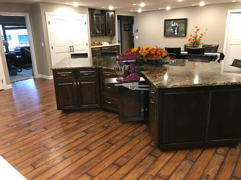 Large traditional galley open plan kitchen in Other with raised-panel cabinets, granite benchtops, stainless steel appliances, an undermount sink, dark wood cabinets, dark hardwood floors, with island and brown floor.