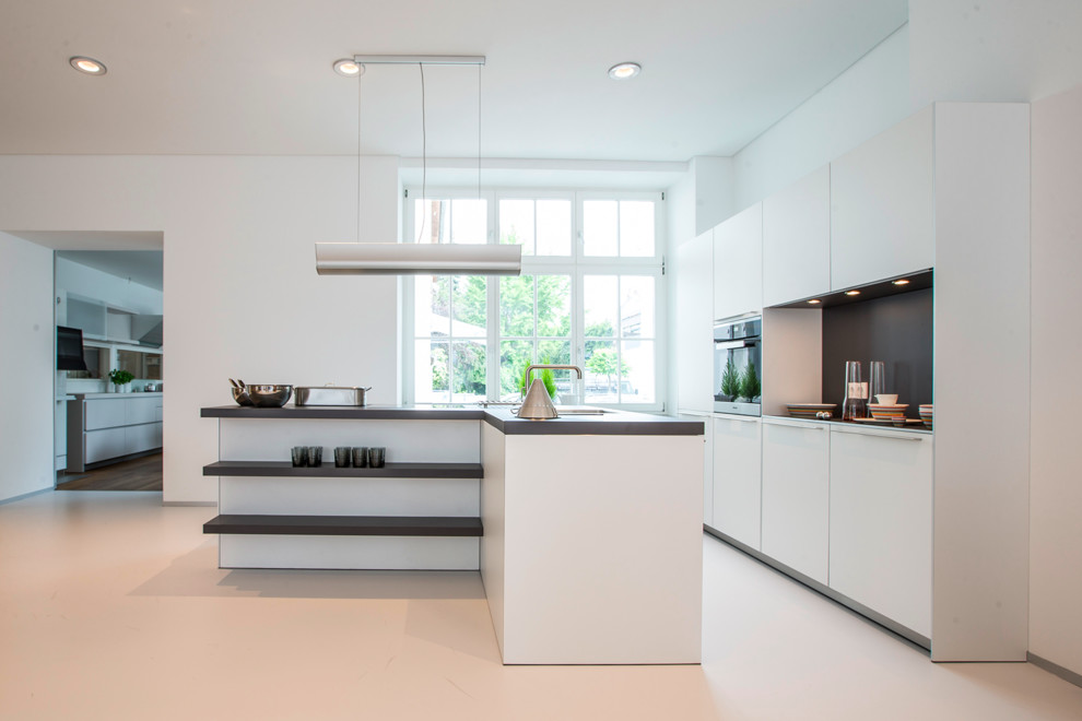 Design ideas for a large contemporary open plan kitchen in Frankfurt with flat-panel cabinets, white cabinets, grey splashback, black appliances and with island.