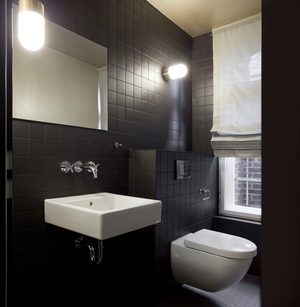 This is an example of a small contemporary powder room in Berlin with a wall-mount sink, black walls, a wall-mount toilet and black tile.