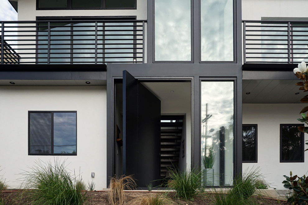 Photo of an expansive modern front door in San Diego with white walls, a pivot front door and a black front door.
