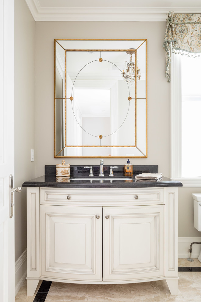 Mid-sized traditional powder room in Toronto with furniture-like cabinets, white cabinets, beige tile, stone tile, marble floors, granite benchtops, an undermount sink and beige walls.