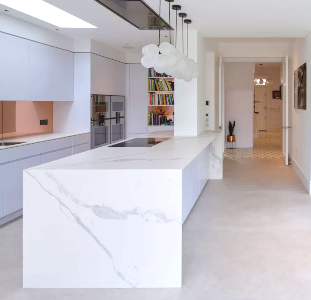 Photo of a large contemporary galley eat-in kitchen in London with an integrated sink, flat-panel cabinets, white cabinets, marble benchtops, metallic splashback, glass sheet splashback, black appliances, concrete floors, with island, grey floor and white benchtop.