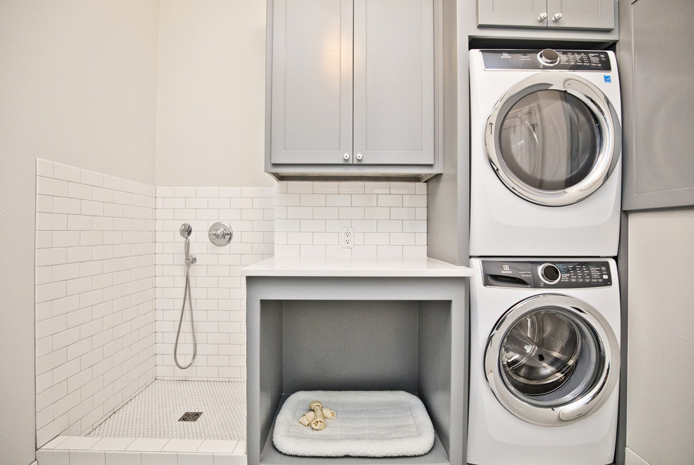 Example of a mid-sized transitional single-wall dedicated laundry room design with shaker cabinets, gray cabinets, gray walls, a stacked washer/dryer and white countertops