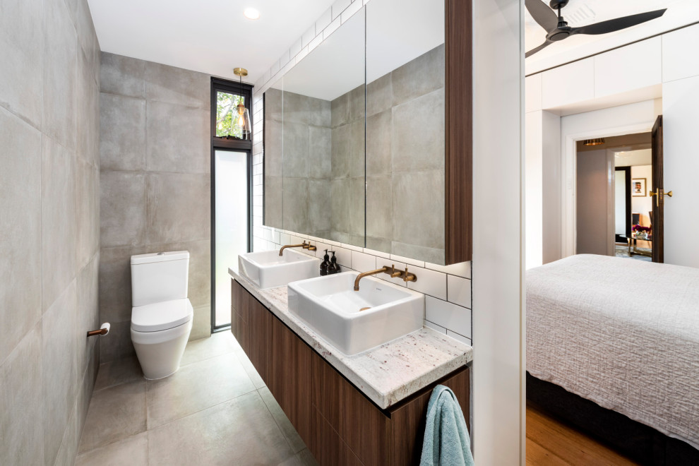 Mid-sized contemporary master bathroom in Melbourne with flat-panel cabinets, medium wood cabinets, a corner tub, an open shower, a two-piece toilet, gray tile, porcelain tile, grey walls, porcelain floors, a vessel sink, granite benchtops, grey floor, an open shower and white benchtops.