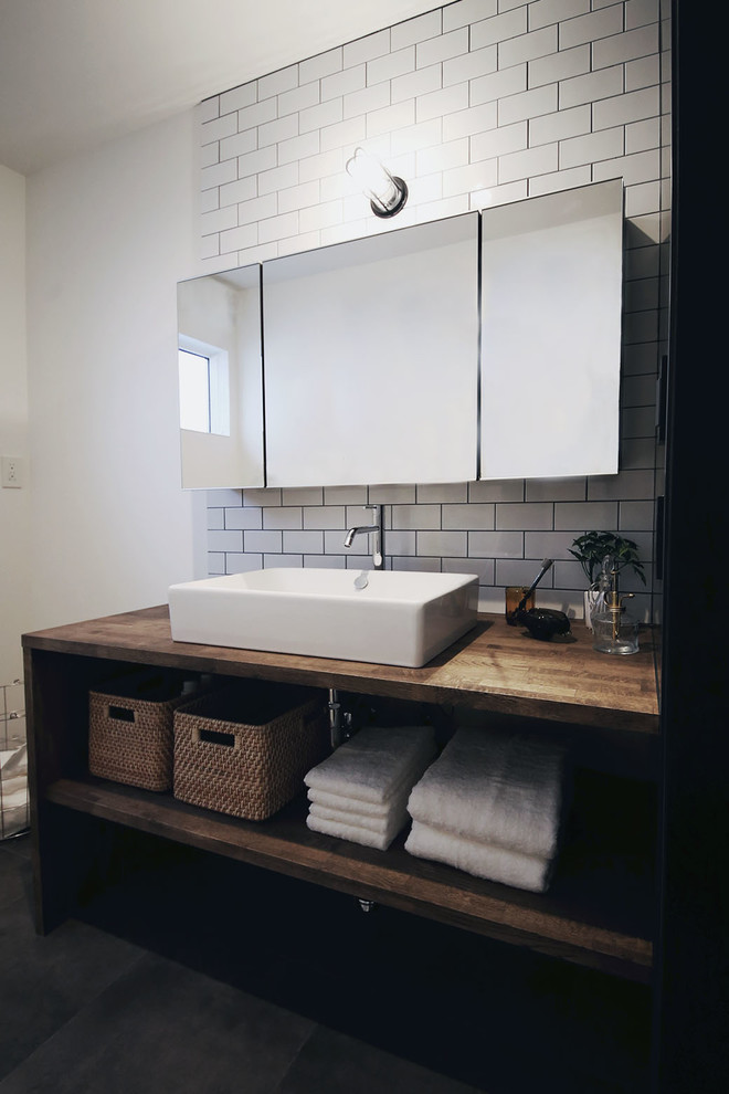 Photo of an industrial powder room in Nagoya with open cabinets, dark wood cabinets, white tile, white walls, a vessel sink, wood benchtops, black floor and brown benchtops.