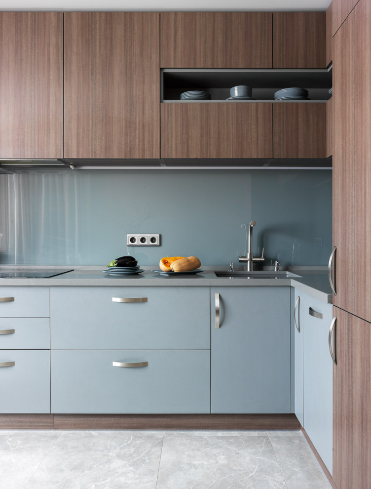 This is an example of a contemporary l-shaped kitchen in Moscow with an undermount sink, flat-panel cabinets, blue cabinets, stainless steel benchtops, glass sheet splashback, stainless steel appliances, no island, grey floor and grey benchtop.