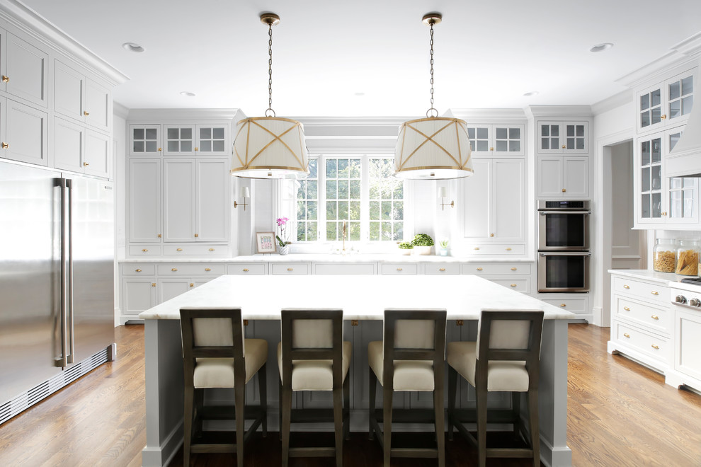 Photo of a traditional separate kitchen in Nashville with shaker cabinets, white cabinets, window splashback, stainless steel appliances, medium hardwood floors, with island and marble benchtops.