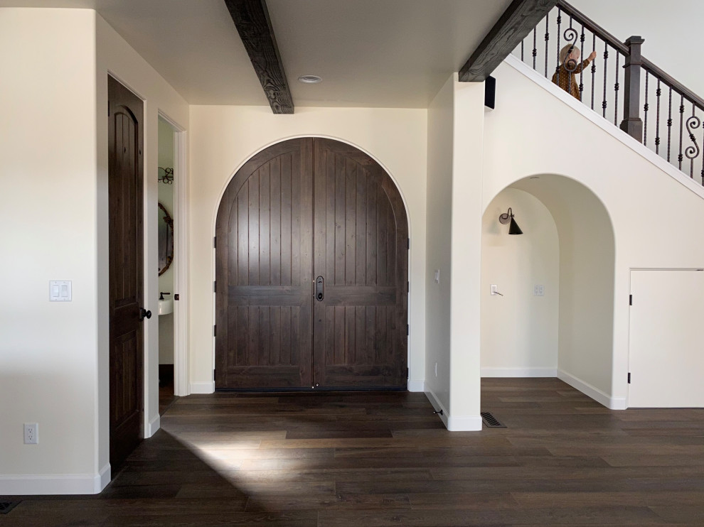 Modelo de puerta principal mediterránea grande con paredes blancas, suelo de madera oscura, puerta doble, puerta de madera oscura, suelo marrón y vigas vistas