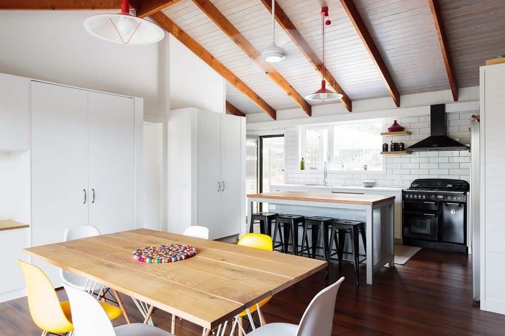 This is an example of a contemporary l-shaped eat-in kitchen in Canberra - Queanbeyan with white cabinets, wood benchtops, white splashback, subway tile splashback, black appliances, medium hardwood floors and with island.