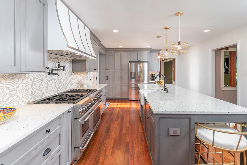 This is an example of a transitional eat-in kitchen in Philadelphia with a farmhouse sink, recessed-panel cabinets, grey cabinets, quartz benchtops, grey splashback, cement tile splashback, stainless steel appliances, medium hardwood floors, with island and white benchtop.