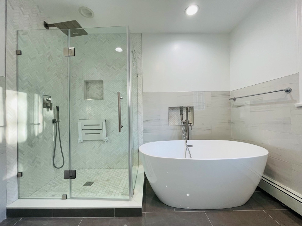 This is an example of a large modern master wet room bathroom in New York with shaker cabinets, grey cabinets, a freestanding tub, a one-piece toilet, gray tile, matchstick tile, white walls, ceramic floors, an undermount sink, granite benchtops, grey floor, a hinged shower door, white benchtops, a shower seat, a double vanity, a freestanding vanity and vaulted.