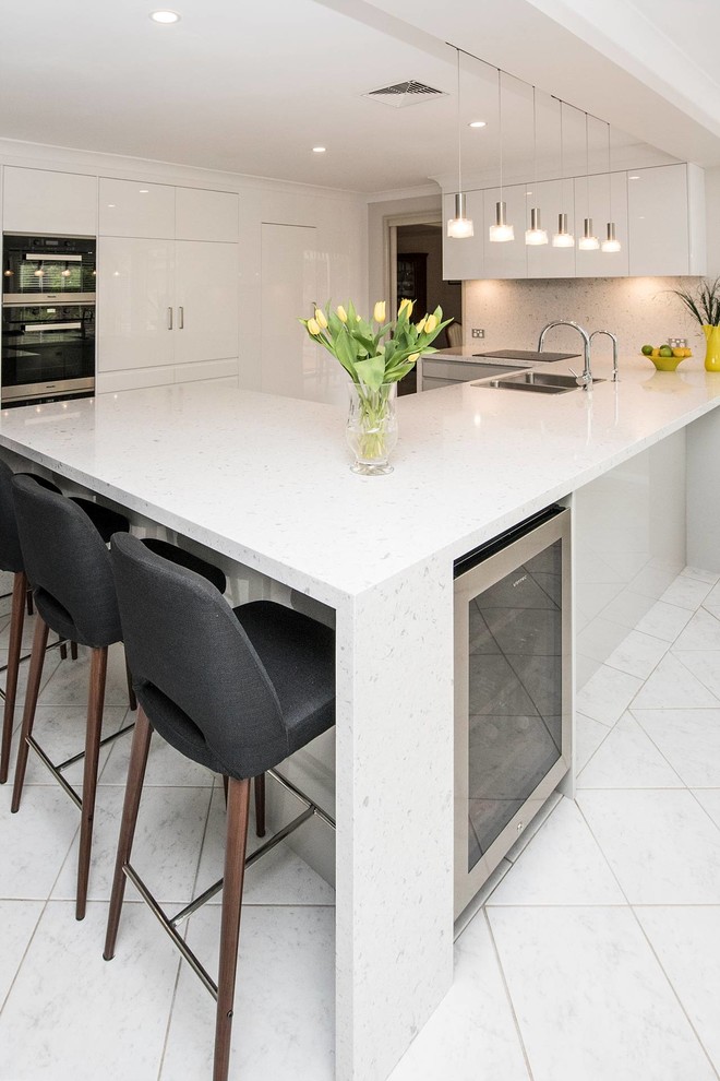 Large contemporary u-shaped open plan kitchen in Sydney with a drop-in sink, flat-panel cabinets, white cabinets, quartz benchtops, marble splashback, stainless steel appliances, ceramic floors, with island, grey splashback and grey benchtop.