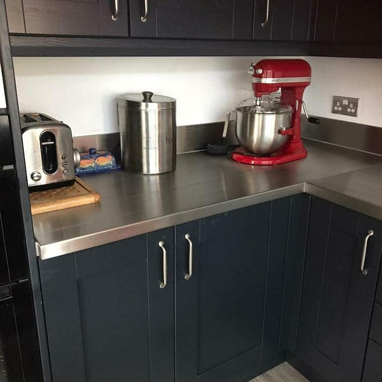 Foto på ett mellanstort funkis kök, med en integrerad diskho, skåp i shakerstil, grå skåp, bänkskiva i rostfritt stål, svart stänkskydd, stänkskydd i glaskakel, svarta vitvaror, laminatgolv, en halv köksö och grått golv