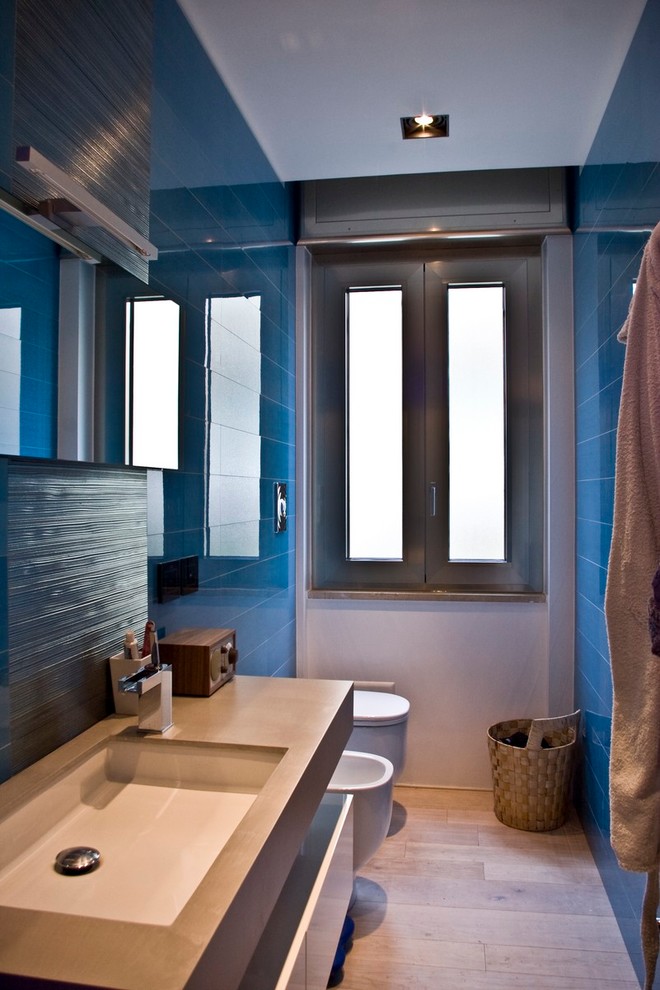 This is an example of a small contemporary bathroom in Naples with flat-panel cabinets, light wood cabinets, a two-piece toilet, blue tile, porcelain tile, white walls, light hardwood floors, a drop-in sink and engineered quartz benchtops.