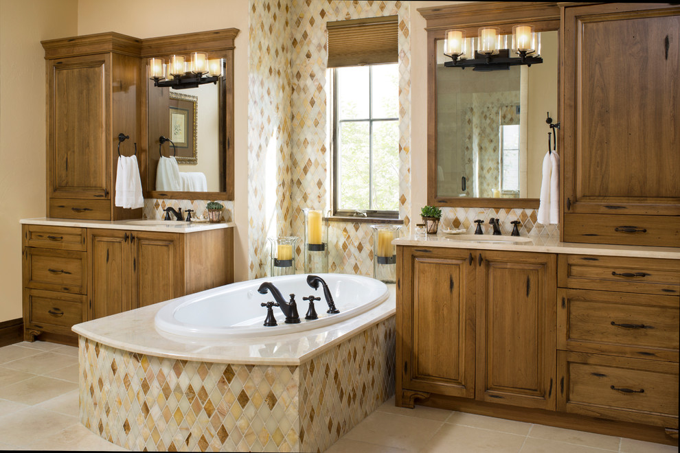 Large mediterranean master bathroom in Denver with raised-panel cabinets, distressed cabinets, marble benchtops, multi-coloured tile, stone tile, a drop-in tub, an undermount sink, beige walls and travertine floors.