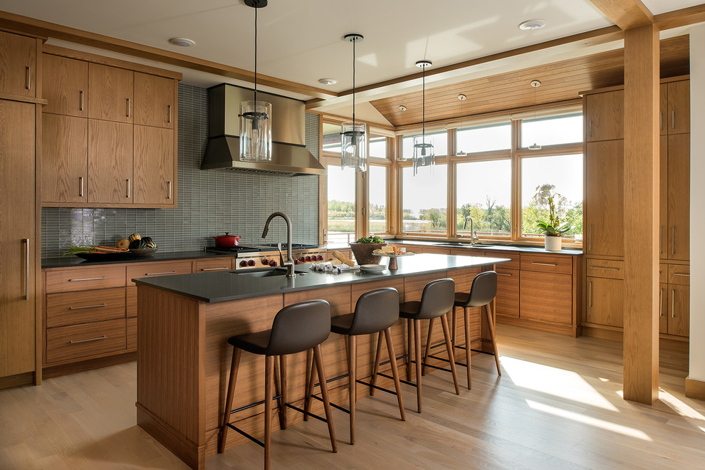 Photo of a contemporary l-shaped kitchen in Minneapolis with an undermount sink, flat-panel cabinets, medium wood cabinets, grey splashback, glass tile splashback, panelled appliances, light hardwood floors, with island and beige floor.