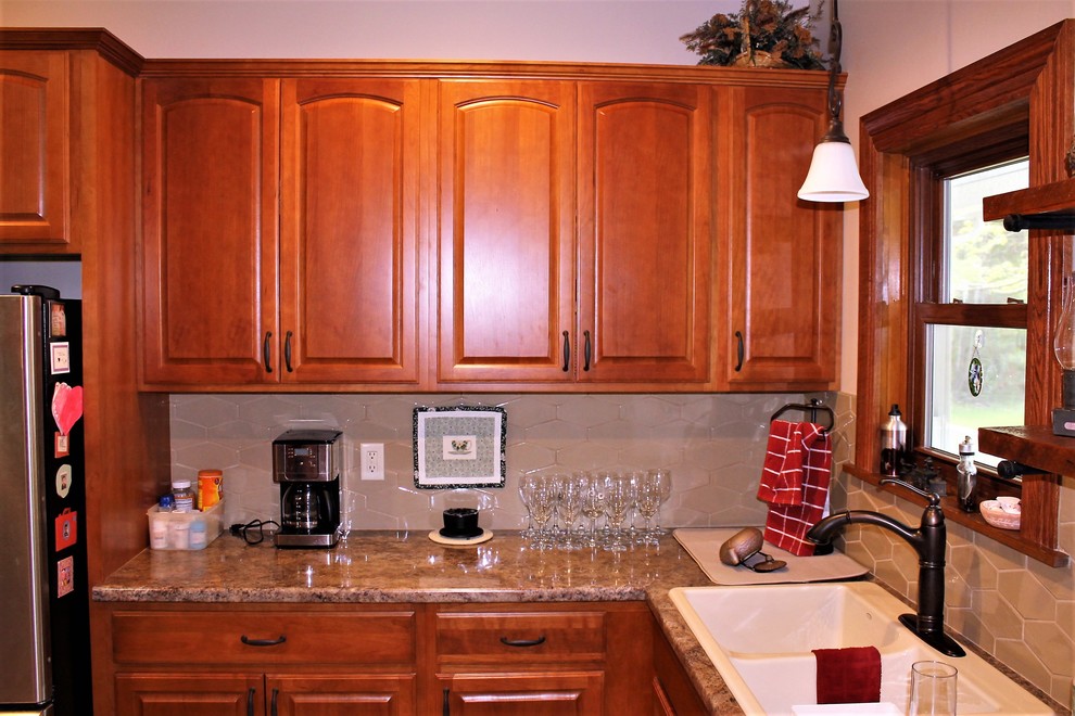 Example of a mid-sized mountain style l-shaped vinyl floor and beige floor eat-in kitchen design with a farmhouse sink, raised-panel cabinets, medium tone wood cabinets, laminate countertops, beige backsplash, cement tile backsplash, stainless steel appliances, a peninsula and beige countertops
