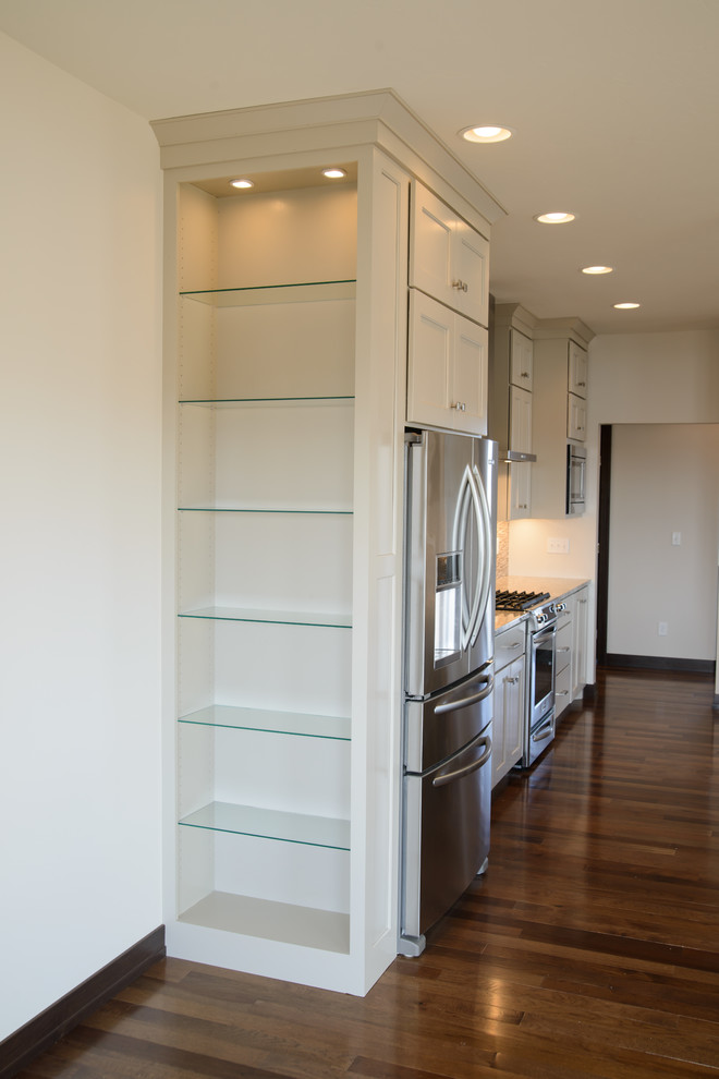 Transitional l-shaped medium tone wood floor open concept kitchen photo with a farmhouse sink, shaker cabinets, white cabinets, stainless steel appliances and an island