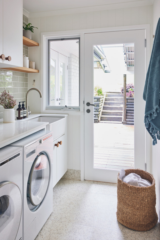 Inspiration for a contemporary single-wall dedicated laundry room in Sydney with a farmhouse sink, flat-panel cabinets, white cabinets, grey splashback, subway tile splashback, white walls, beige floor, white benchtop and planked wall panelling.