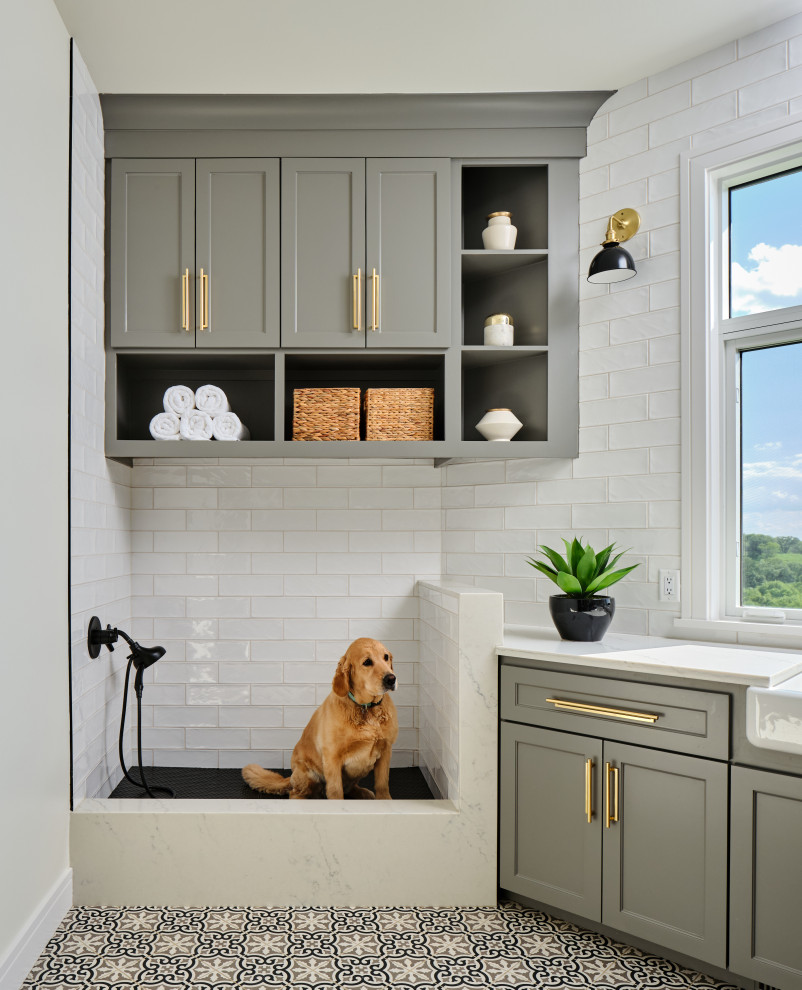 Mid-sized transitional u-shaped dedicated laundry room in Omaha with a farmhouse sink, shaker cabinets, grey cabinets, quartz benchtops, white splashback, subway tile splashback, white walls, porcelain floors, a side-by-side washer and dryer, multi-coloured floor and grey benchtop.