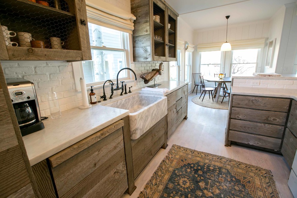 This is an example of a mid-sized arts and crafts galley kitchen in Other with a farmhouse sink, flat-panel cabinets, distressed cabinets, marble benchtops, white splashback, cement tile splashback and light hardwood floors.
