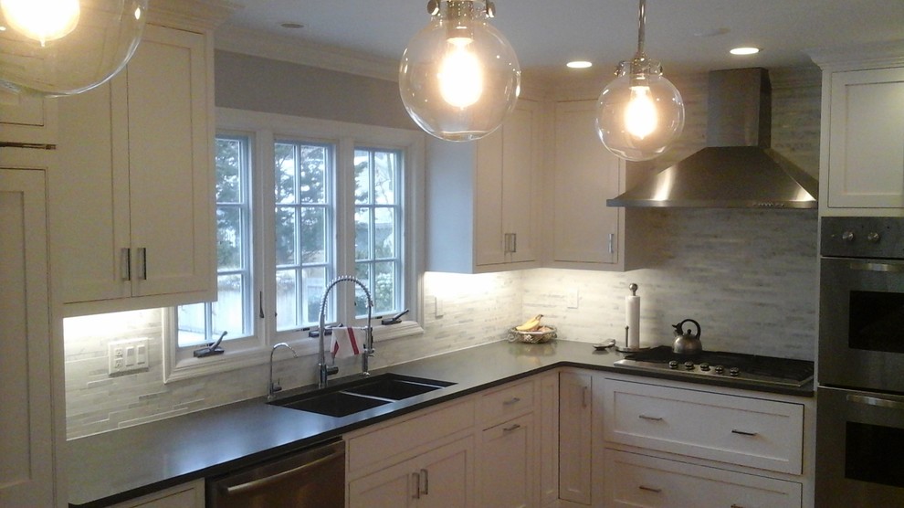 Inspiration for a mid-sized transitional l-shaped light wood floor eat-in kitchen remodel in Newark with a double-bowl sink, shaker cabinets, white cabinets, solid surface countertops, multicolored backsplash, stone tile backsplash, stainless steel appliances and an island