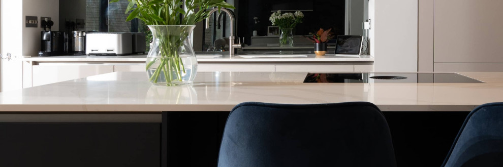 Idee per una cucina minimalista di medie dimensioni con lavello integrato, ante lisce, ante bianche, top in quarzite, elettrodomestici neri, parquet chiaro, pavimento marrone e top bianco