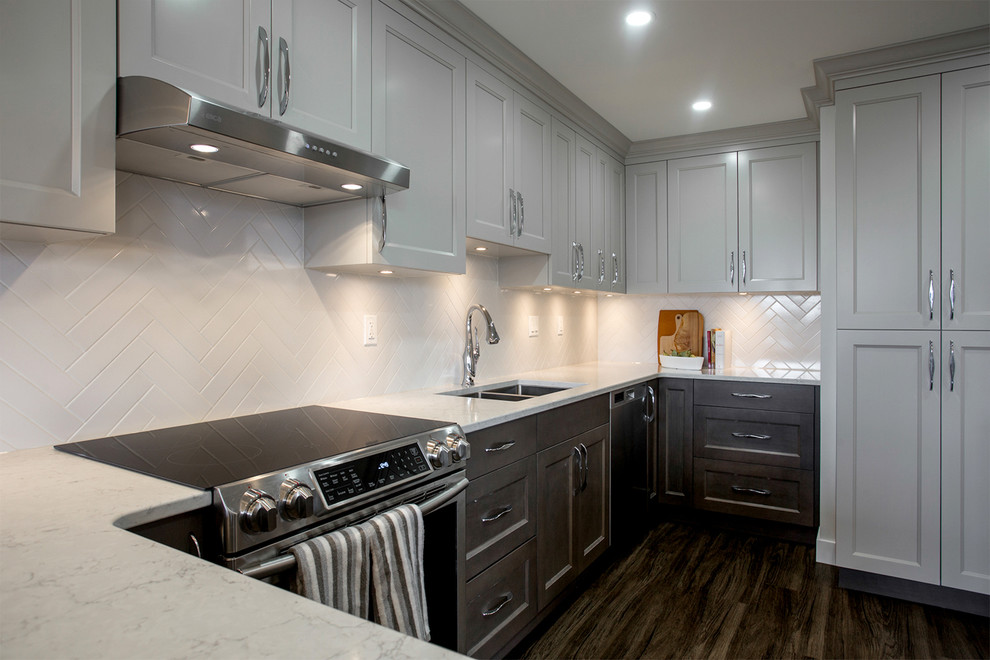 This is an example of a mid-sized transitional u-shaped separate kitchen in Vancouver with an undermount sink, shaker cabinets, grey cabinets, solid surface benchtops, white splashback, timber splashback, stainless steel appliances, dark hardwood floors, a peninsula, brown floor and white benchtop.
