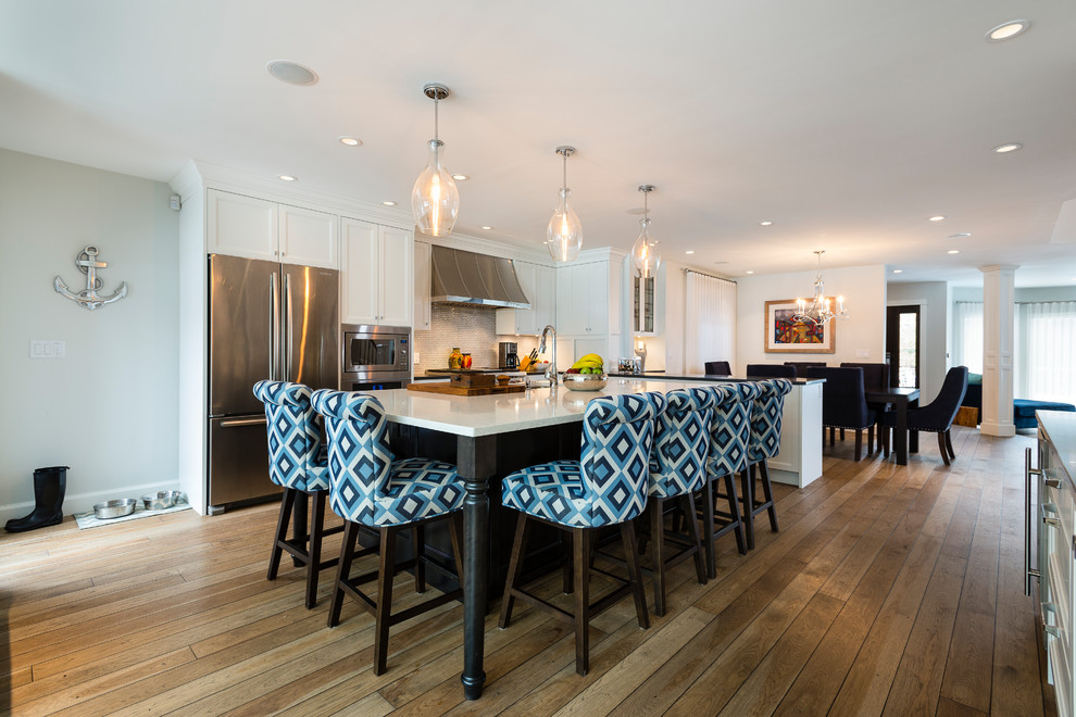 This is an example of a mid-sized transitional l-shaped open plan kitchen in Vancouver with an undermount sink, shaker cabinets, white cabinets, quartz benchtops, white splashback, mosaic tile splashback, stainless steel appliances, light hardwood floors and with island.