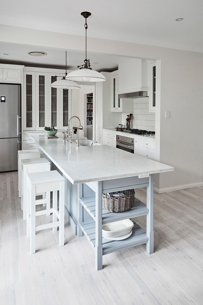 Mid-sized traditional u-shaped kitchen pantry in Sydney with a farmhouse sink, shaker cabinets, white cabinets, marble benchtops, white splashback, subway tile splashback, stainless steel appliances, light hardwood floors and with island.