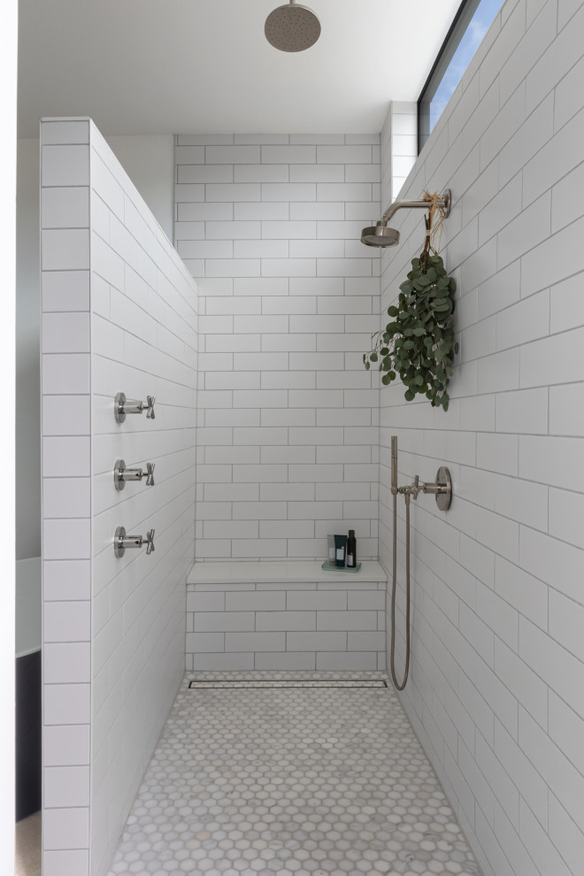 Cette image montre une salle de bain principale nordique avec une baignoire indépendante, une douche ouverte, un carrelage blanc, des carreaux de céramique, un mur blanc, sol en béton ciré, un sol gris, une cabine de douche à porte battante et un banc de douche.