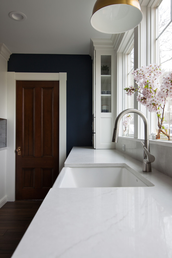 Example of a large transitional l-shaped enclosed kitchen design in Boston with a farmhouse sink, shaker cabinets, white cabinets, quartz countertops, white backsplash, stainless steel appliances, an island and white countertops