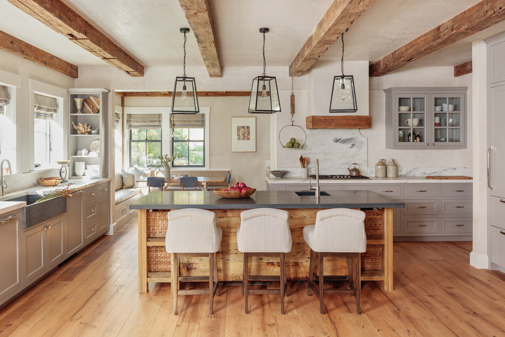 Photo of a country u-shaped kitchen in Boston with a farmhouse sink, shaker cabinets, grey cabinets, white splashback, stone slab splashback, panelled appliances, medium hardwood floors, with island, brown floor and white benchtop.