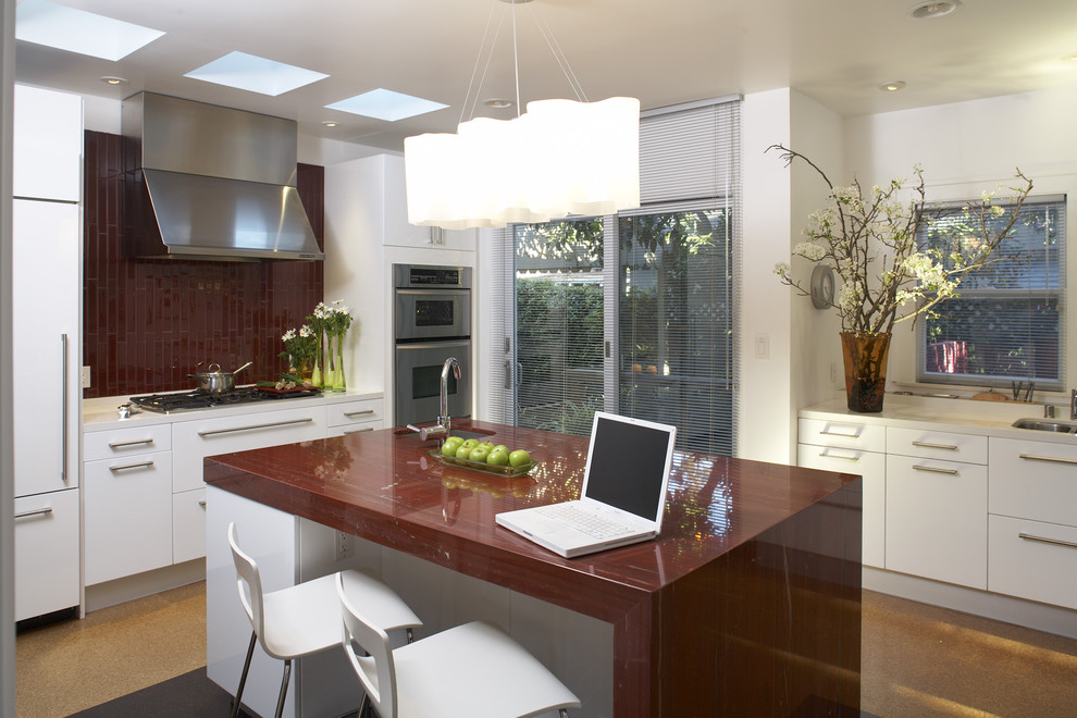 Mid-sized modern u-shaped eat-in kitchen in San Francisco with a drop-in sink, flat-panel cabinets, white cabinets, granite benchtops, red splashback, ceramic splashback, stainless steel appliances, cork floors, with island and orange floor.
