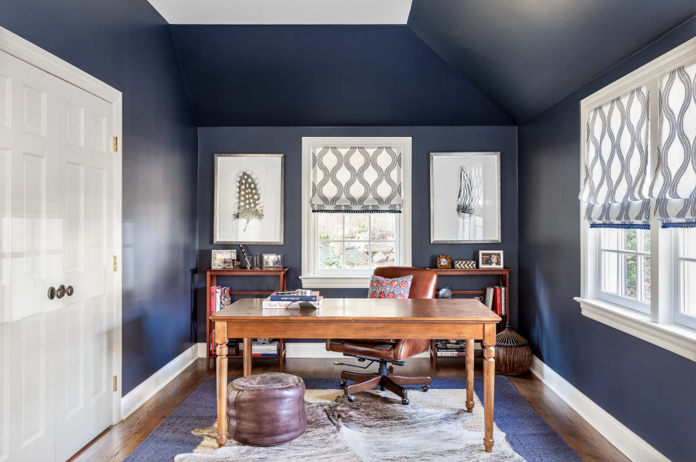 This is an example of a beach style home office in New York with blue walls, dark hardwood floors, a freestanding desk, brown floor and vaulted.